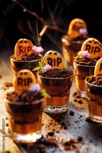 Halloween funny food idea for  party, graveyard chocolate-caramel mousse with addition crushed cookies in small glass cups, focus on the dessert inside.  