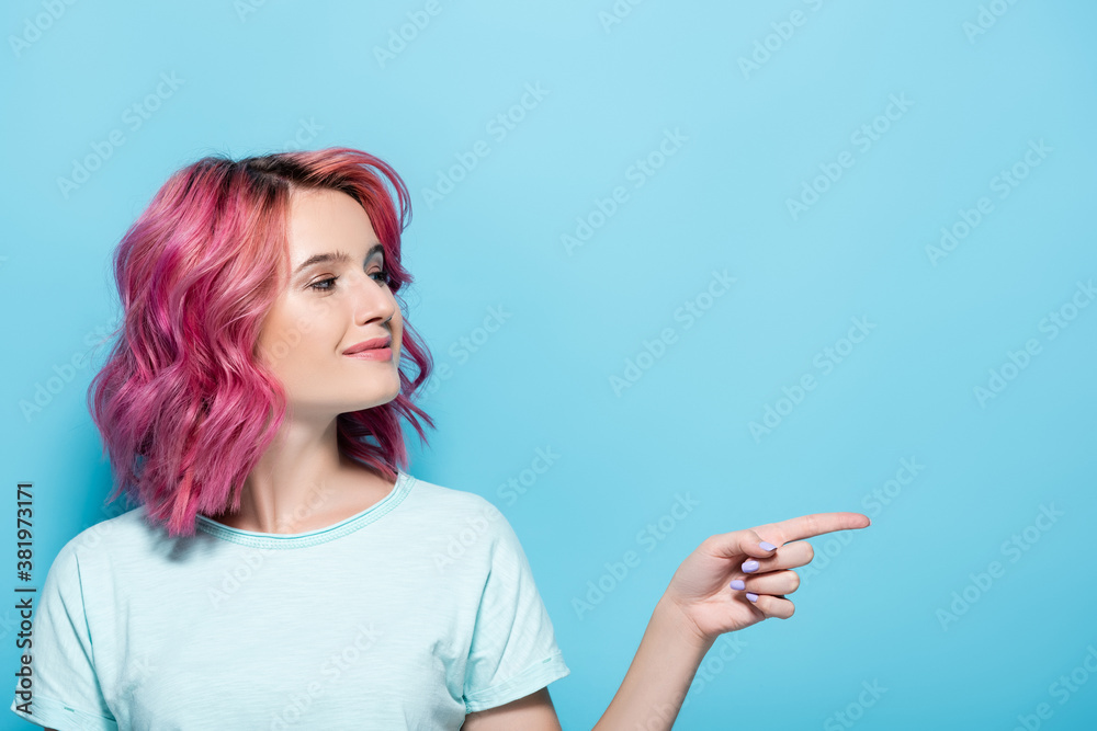 young woman with pink hair pointing aside on blue background young woman with pink hair pointing aside on blue background