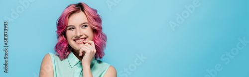 young woman with pink hair smiling and flirting isolated on blue, panoramic shot