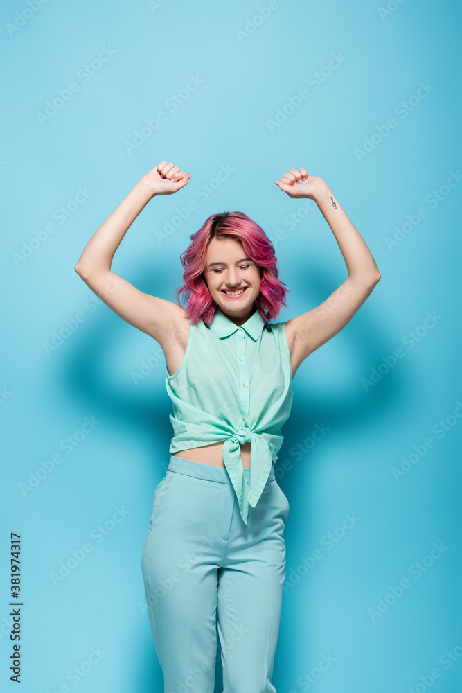 young woman with pink hair and hands in air smiling on blue background young woman with pink hair and hands in air smiling on blue background