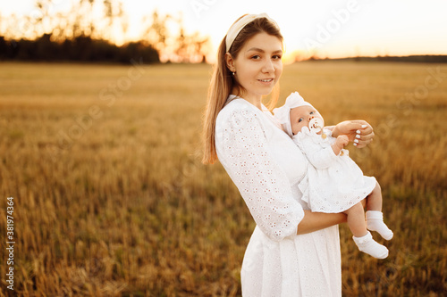 Portrait of gorgeous mother with beautiful little daughter at the field, tender mom hold cute newborn baby girl in arms, smiling, happy family moments, maternity concept 