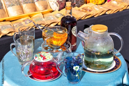 Glass teapot and cups with different kinds of herbal tea on the table in a street market 