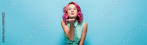 young woman with pink hair blowing kiss on blue background, panoramic shot