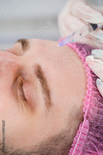 Beautician woman doing ultrasound facial cleaning procedure for young man in clinic. Closeup and hand client portrait, closeup side view. Procedure in the beauty salon.