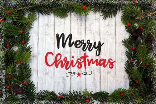 Weihnachtshintergrund, Konzept mit Rahmen aus grünen Nadelzweigen, Text Frohe Weihnachten, weißes Holz, Beeren, Früchte, Dekoration. © Oda Hoppe