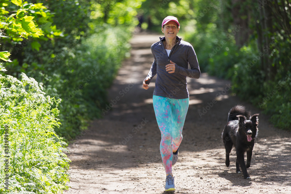 © Paul Bradbury/Caia Image - Woman jogging with dog on sunny trail © Paul Bradbury/Caia Image - Woman jogging with dog on sunny trail