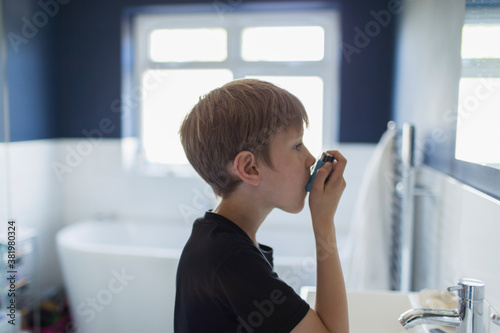 Boy with asthma using inhaler in bathroom photo