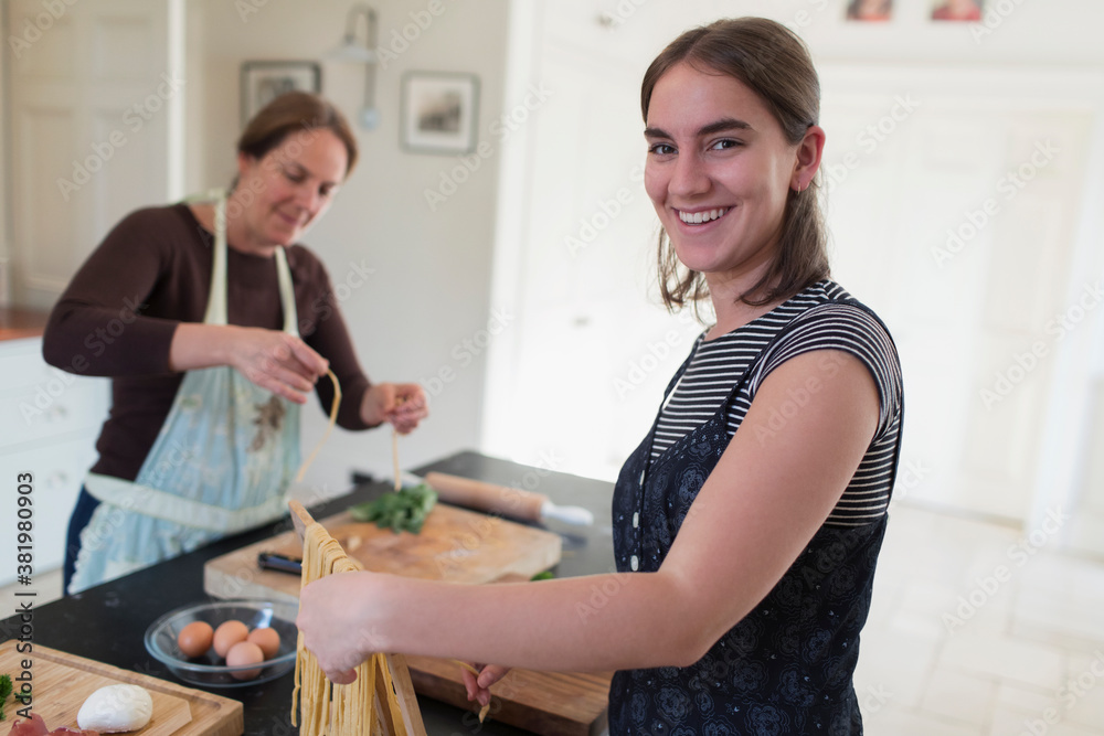 Portrait happy teenage girl making homemade pasta with mother at home Portrait happy teenage girl making homemade pasta with mother at home