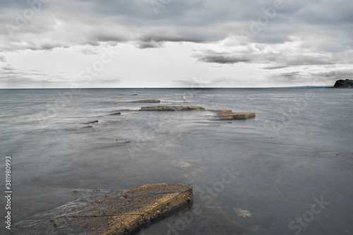 Long exposure shot of rocks sticking out of water and adramatic sky, calm waves and sharp rock formations, beautiful ocean and sky view in Kimmeridge Bay UK photo