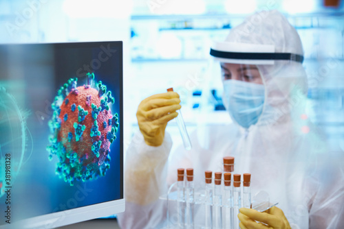 Female scientist in clean suit with test tubes studying coronavirus photo