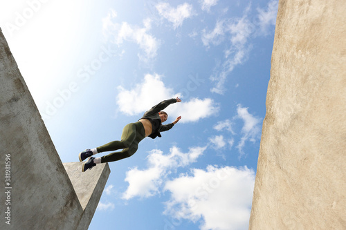A girl jumps from a wall against a blue sky