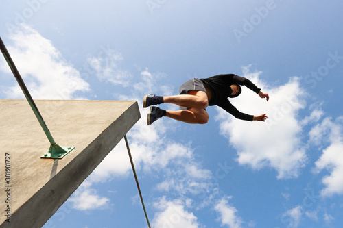 The guy is engaged in parkour jumping from the wall against the blue sky