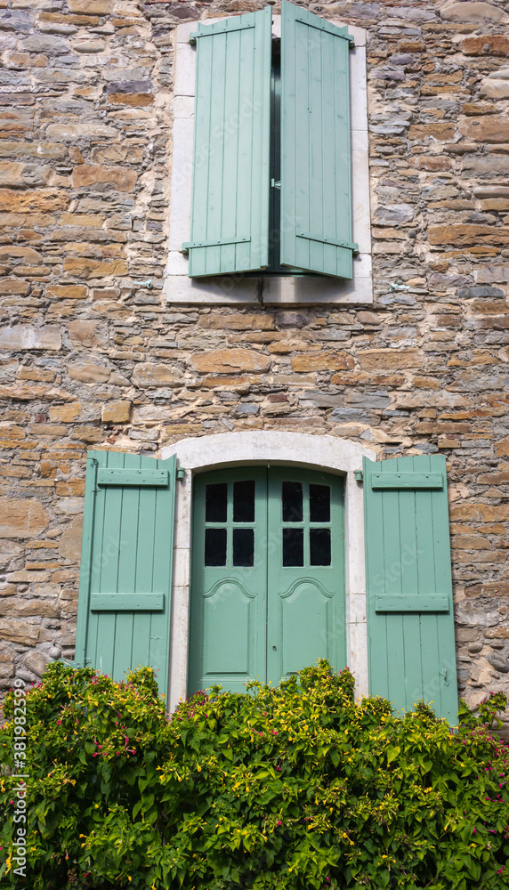 Old house with windows and green shutters. Traditional exterior of rural house, France. Facade of medieval stone building with flowers. Retro residential design. French traditional architecture. 