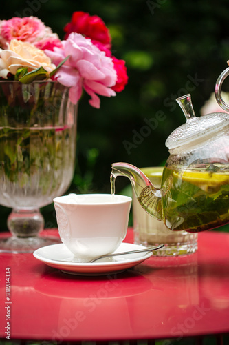 Pouring green tea in white cup on table with roses