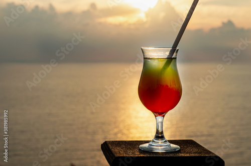 Colorful alcoholic exotic cocktail in a glass isolated against the background of the Mediterranean Sea in the rays of sunset sun. Big plan. Romantic background with the ability to insert text.