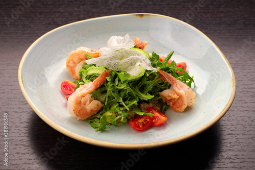 Salad with shrimps, tomatoes and arugula, on a white plate, on a dark background