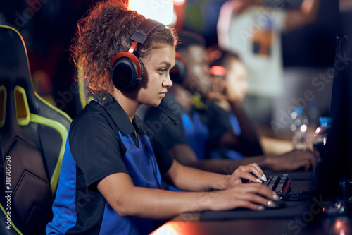 Side view of a focused mixed race girl, female cybersport gamer wearing headphones playing online video games, participating in eSport tournament