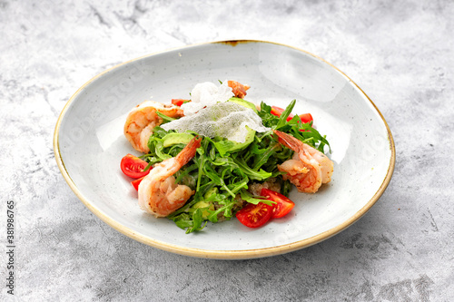 Salad with shrimps, tomatoes and arugula, on a white plate, on a light background