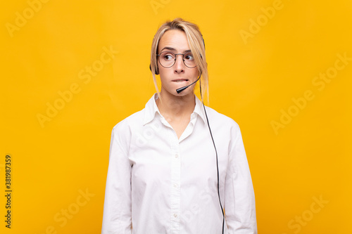 young woman telemarketer looking puzzled and confused, biting lip with a nervous gesture, not knowing the answer to the problem