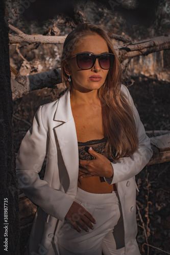 fashionable attractive woman in a white suit and sunglasses on a background of white trees in the forest © Ruslan