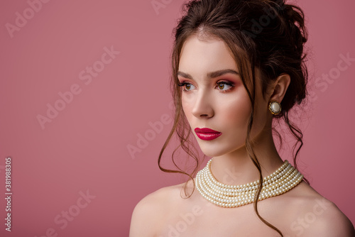Beauty, fashion portrait of young beautiful woman with pink, fuchsia, color eyes, lips makeup, wearing elegant white pearl necklace, earrings, posing on pink background. Copy, empty space for text
