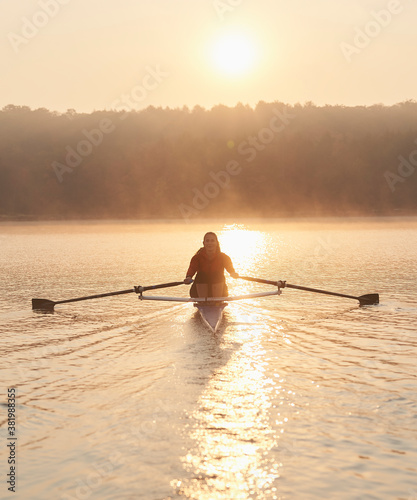 Middle aged woman rowing on calm autumn lake at early morning with mist over water. photo