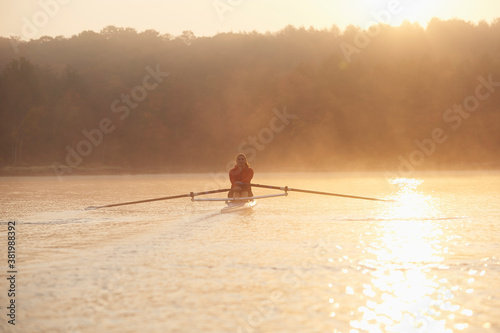 Middle aged woman rowing on calm autumn lake at early morning with mist over water.