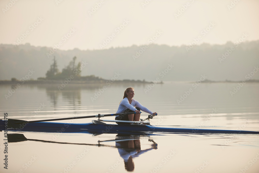 Middle aged woman rowing on calm autumn lake at early morning with mist over water. Middle aged woman rowing on calm autumn lake at early morning with mist over water.