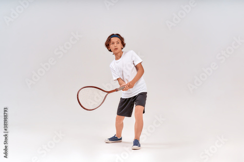 Tennis training. Full-length shot of a teenage boy holding tennis racket and looking away isolated over grey background © Kostiantyn