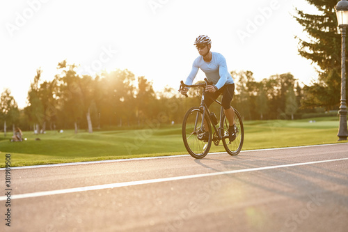 Perfect cycling season. Athletic man in sportswear, professional bicycle racer in sportswear riding mountain road bike in the city park at sunset
