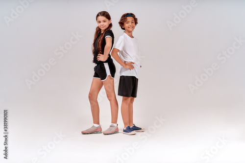 Children engaged in sport. Two teenagers, cute boy and girl in sportswear looking at camera and smiling while posing isolated over grey background