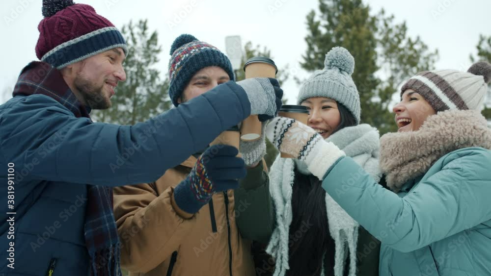 Cheerful girls and guys are enjoying winter day outdoors clinking coffee cups laughing in park having fun together celebrating enjoyable meeting Cheerful girls and guys are enjoying winter day outdoors clinking coffee cups laughing in park having fun together celebrating enjoyable meeting