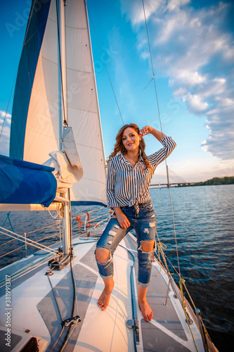 Beautiful young woman in jeans and a shirt posing on yacht On the Sunset. Model is sailing on board.
