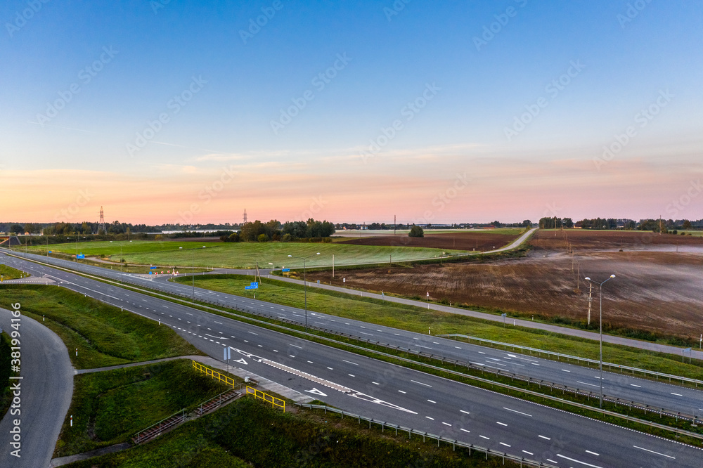 Fototapeta premium Aerial view of a highway passing through agricultural fields at sunrise
