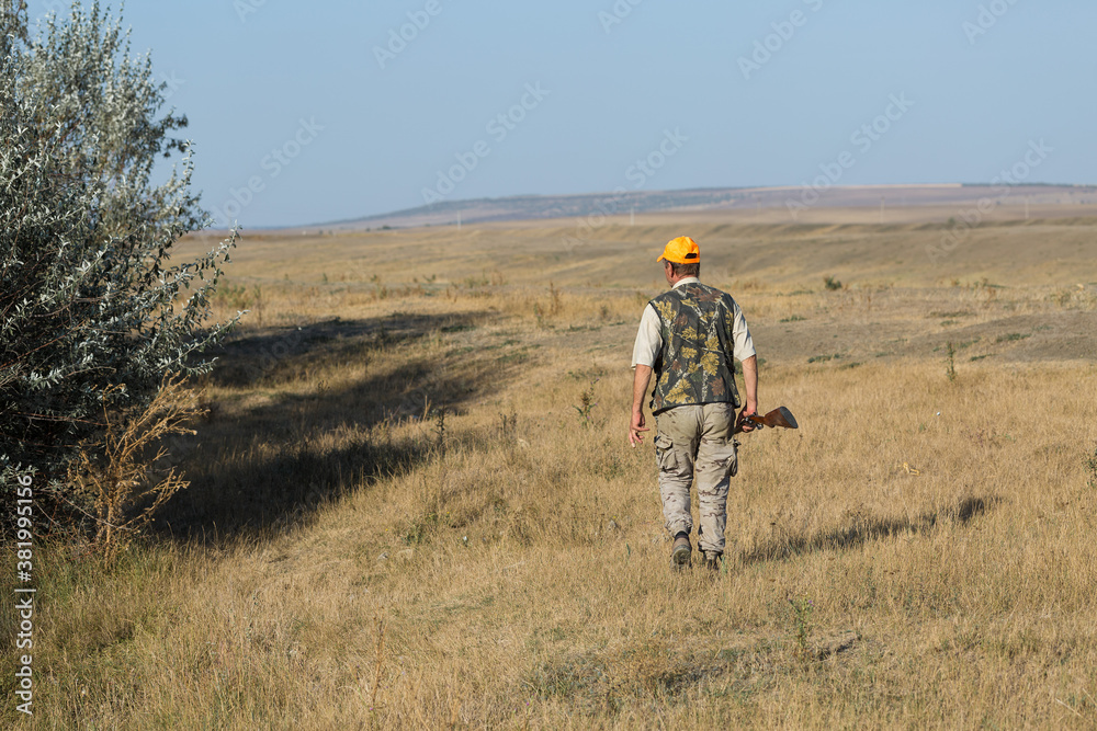 Duck hunter with shotgun walking through a meadow. .Rear view of a man with a weapon in his hands.