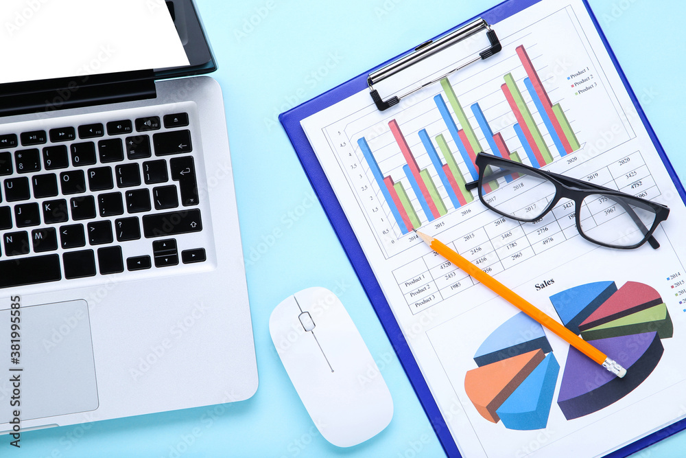 Laptop computer with paper charts and glasses on blue background Laptop computer with paper charts and glasses on blue background