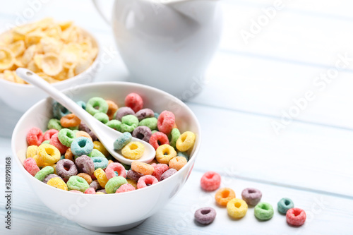 Colorful corn rings in bowl with spoon on white wooden table