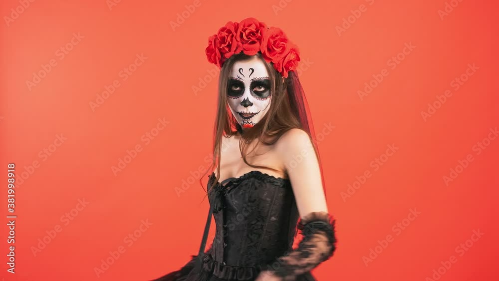 Day of Dead, lady with sugar skull make-up dancing, performing curtsy and smiling posing on red background, Halloween