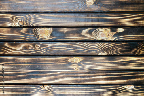 Old burnt wooden plank dark brown texture background with horizontal boards. Flat lay close-up view.