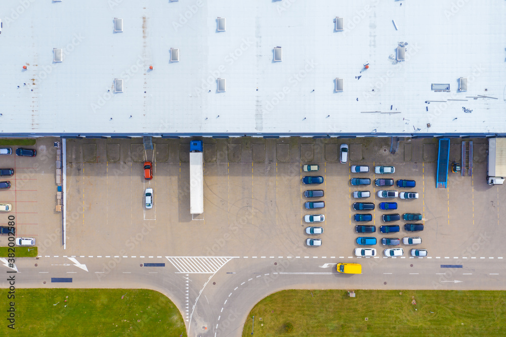 Aerial Top View of Industrial Storage Building Area with Solar Panels on the Roof and Many Trucks Unloading Merchandise.