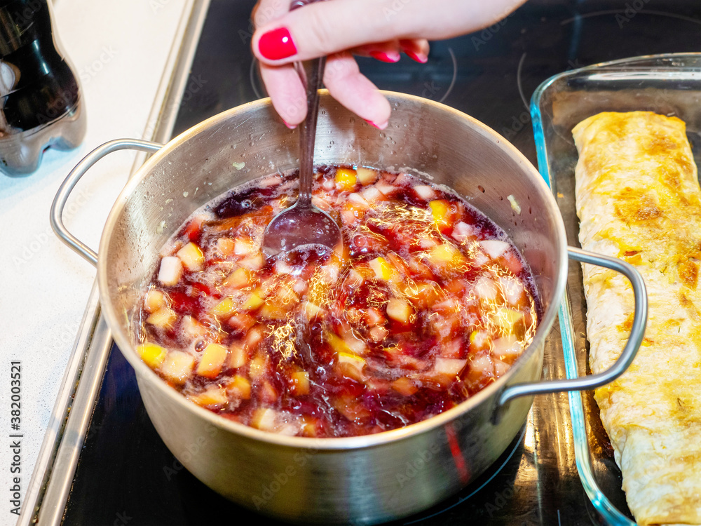 Female hand with red nails stirs mulled wine on a stove with a spoon Female hand with red nails stirs mulled wine on a stove with a spoon
