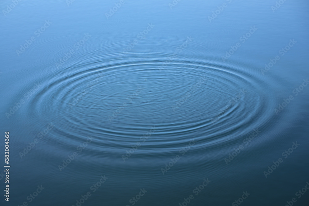 Background from the surface of a water, from which small ripples pull themselves in a circle from the inside out Background from the surface of a water, from which small ripples pull themselves in a circle from the inside out