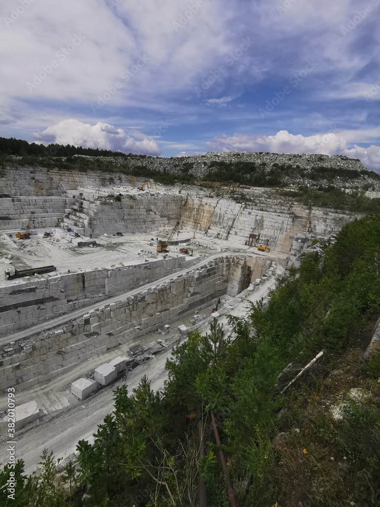 Marble open pit near the Ekaterinburg, Mramorskoe. Broken stone in Ural mountains, Russia. Vertical industry landscape with white stone and sky