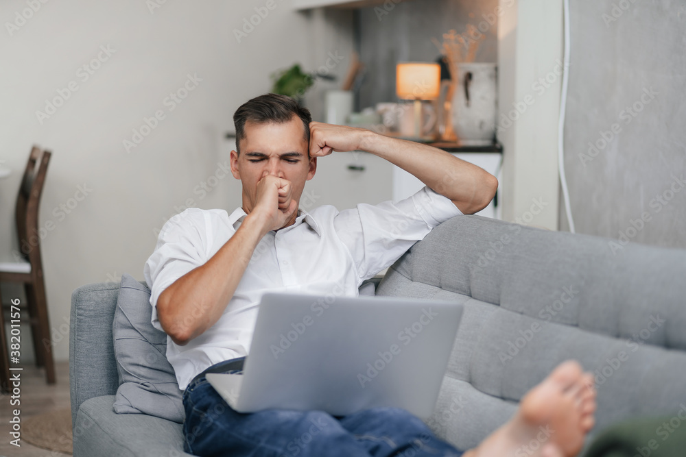 yawning young man with a laptop is resting in the living room. yawning young man with a laptop is resting in the living room.