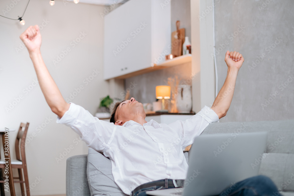 Obraz premium happy young man with a laptop is celebrating sitting on the sofa.
