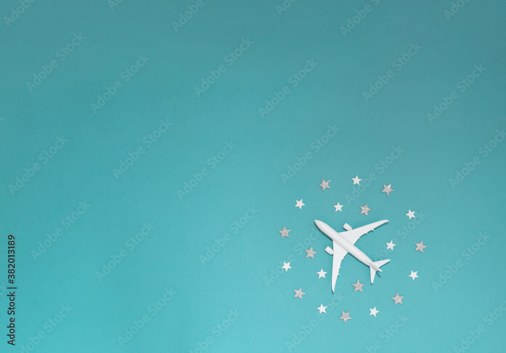 Airplane toy among white and silver stars in a circle on a blue background. With an empty space for text, banner for travel.