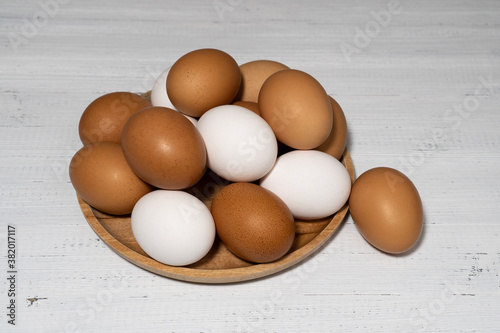 Brown and white raw chicken eggs on wooden plate. Organic eggs on white wood background.