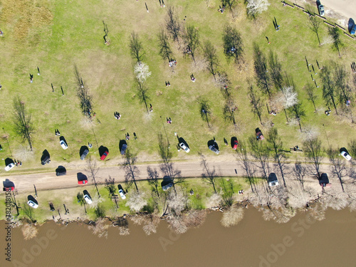 Foto aérea de un parque con automóviles, gente descansando y la costa de un río.  photo