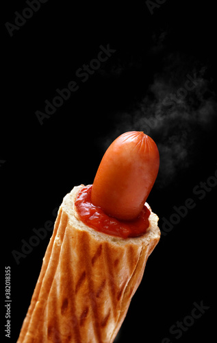 Delicious french hot dog with ketchup on a black background, isolated