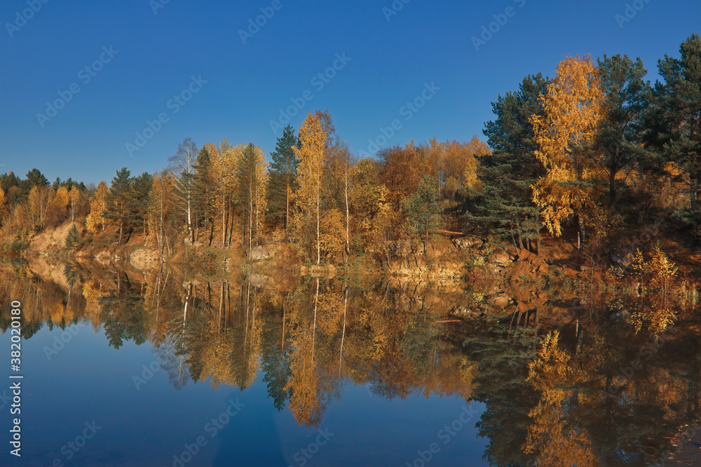 Autumn landscape, forest trees are reflected in calm river water against a background of blue sky and white clouds. Autumn landscape, forest trees are reflected in calm river water against a background of blue sky and white clouds.